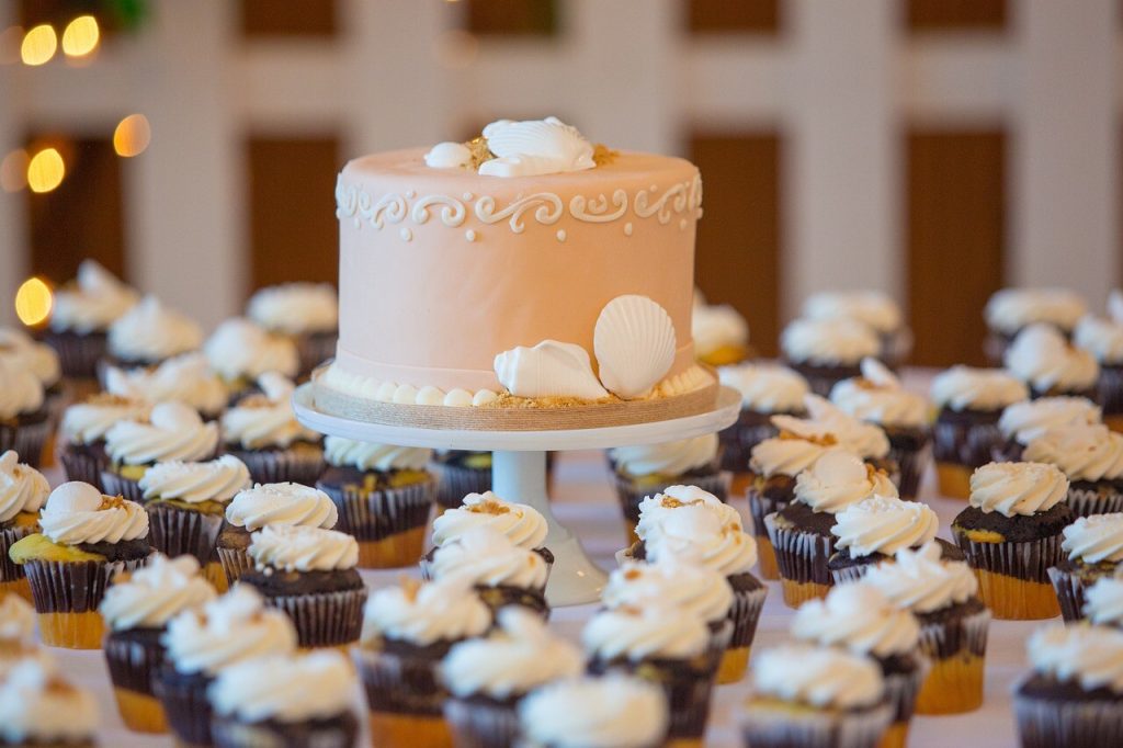 Ferskenfarvet lagkage på fad omgivet af cupcakes