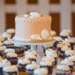 Ferskenfarvet lagkage på fad omgivet af cupcakes