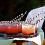 Tjener serverer røde drinks med sugerør på bakke