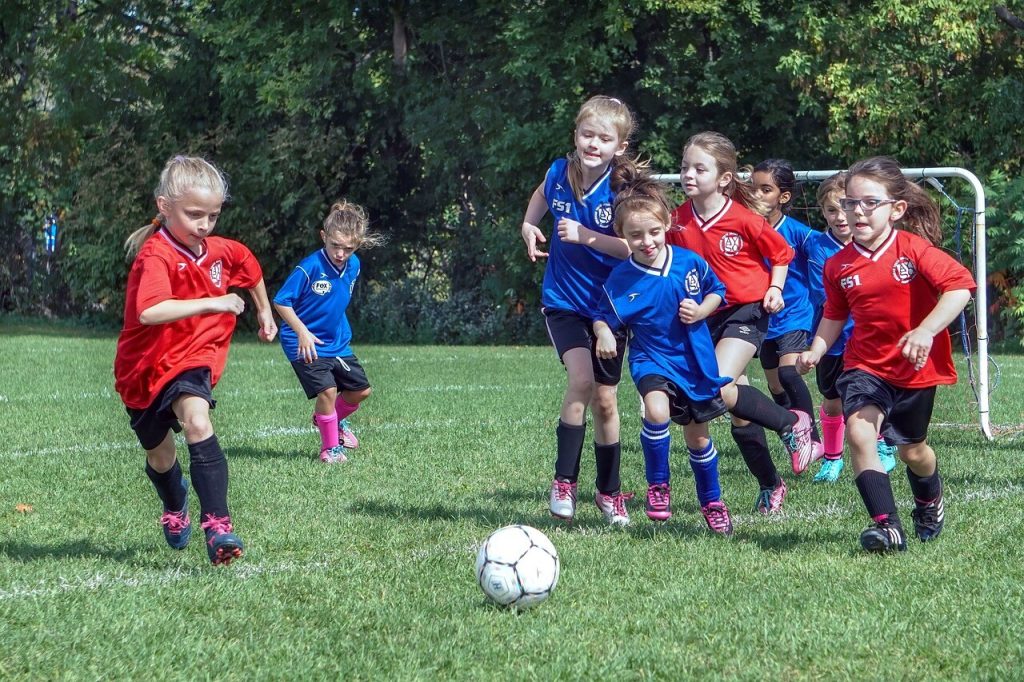 Piger spiller fodbold på græsbane