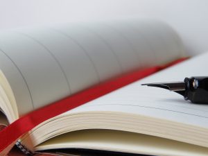 Åben notesbog med fyldepen og rødt bånd